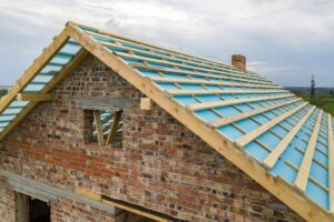 Aerial view of a brick house with wooden roof frame under construction.
