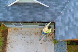 Roofing contractor cleaning clogged gutter during roof inspection before storm season in Texas.