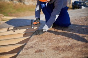 Carpenter hammering nail into OSB panel on the roof top of future cottage. Man worker building wooden frame house. Carpentry and construction concept.