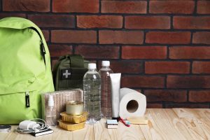 Survival kit. Different emergency supplies on wooden table against brick wall, space for text