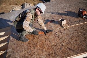 Carpenter hammering nail into OSB panel on the roof top 
