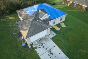 Top view of leaking house roof covered with protective tarp sheets against rain water leaks until replacement of asphalt shingles. Damage of building rooftop as aftermath of hurricane