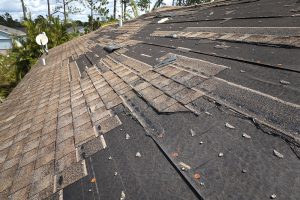 Wind damaged house roof with missing asphalt shingles after hurricane