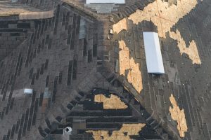 Wind damaged house roof with missing asphalt shingles after hurricane