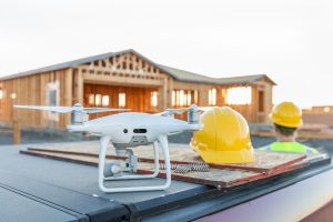 Drone Quadcopter Next to Hard Hat Helmet At Construction Site with Worker Behind.